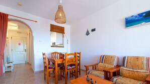 A cozy living room with a wooden dining table, chairs, a sofa, and a hanging light fixture. - Nice apartment for 4 guests with A/C, pool, TV and patio (Calpe)
