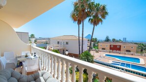 A balcony with a pool, white chairs, and a grey sofa. - Nice apartment for 4 guests with A/C, pool, TV and patio (Calpe)