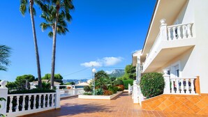 A villa with a tiled patio, white balconies, and a view of the mountains. - Nice apartment for 4 guests with A/C, pool, TV and patio (Calpe)