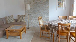 Una sala de estar con una pared de piedra, un sofá, una mesa de centro, una lámpara y una mesa de comedor con sillas.