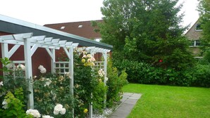 Un jardín con un pérgola blanca, flores en flor y un césped cuidado.