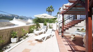 A terrace with white lounge chairs, a large umbrella, and a view of the sea. - Nice apartment in villa for 6 people with WIFI, pool, TV and terrace (Benissa)