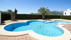 A swimming pool with a unique shape, surrounded by a tiled deck and palm trees. - Nice apartment in villa for 6 people with WIFI, pool, TV and terrace (Benissa)