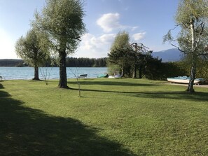 A grassy area with a bench, trees, and a lake.