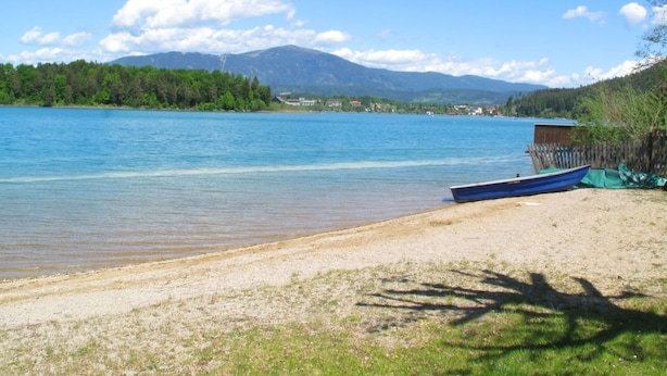 Una playa con un bote en la orilla, una estructura de madera y un área boscosa al fondo.