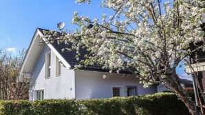 Una casa de dos pisos con una antena parabólica, un cartel con el número 28, y un árbol con flores blancas en el frente.