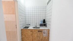 Una cocina pequeña con paredes de azulejos blancos, una encimera de madera, un lavamanos, un microondas y un hervidor.