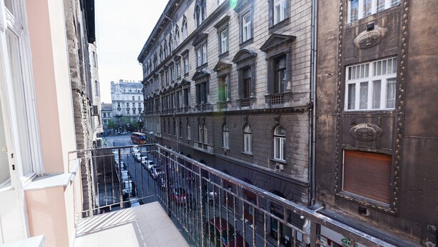 Una calle urbana estrecha flanqueada por edificios, una barandilla metálica y un cielo despejado.