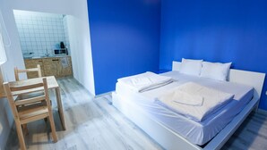 Un dormitorio con una cama grande, una silla de madera y una pequeña kitchenette al fondo.