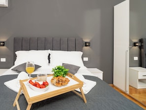 A modern hotel room with a bed, bedside tables, a tray with breakfast items, and a grey wall.