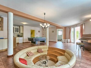 Un vaste espace de vie comprenant une table de billard, un canapé, un piano et un coin repas avec vue.