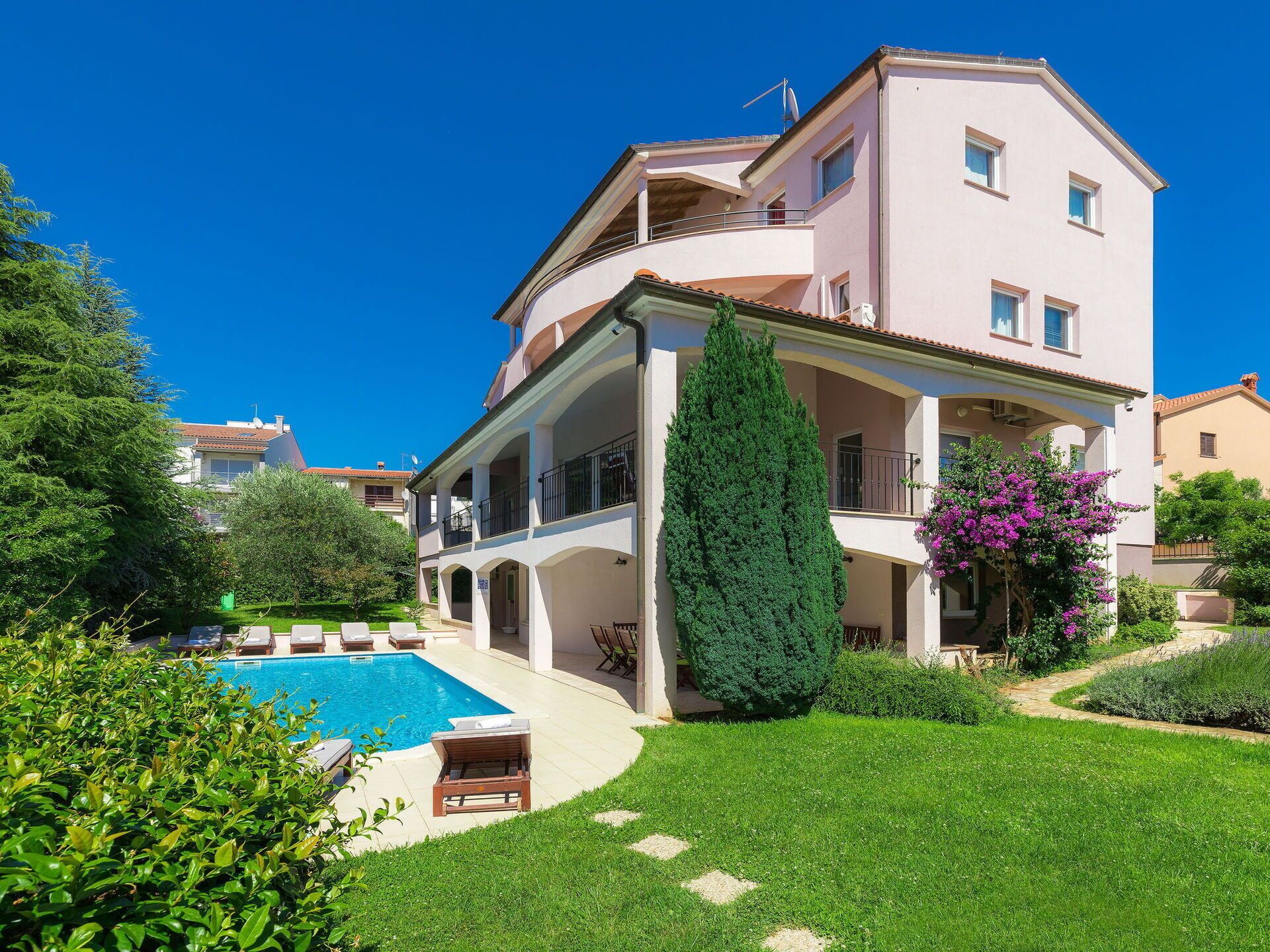 Ein zweistöckiges Haus mit Swimmingpool, umgeben von gepflegten Rasenflächen und einem hohen Baum.
