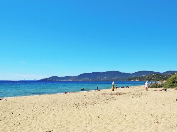 A beach with people sunbathing and swimming, clear blue sky, and mountains in the background.