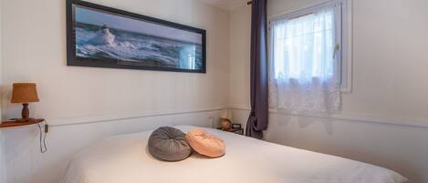 A bedroom with a large bed, a framed picture of the ocean, a lamp, and a window with curtains.