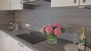 A modern kitchen with a dark countertop, white cabinets, a stainless steel sink, a vase with pink flowers, and a bottle of champagne with glasses on a doily. - Nice apartment for 4 people with WIFI, TV, patio and pets allowed (Wenns)