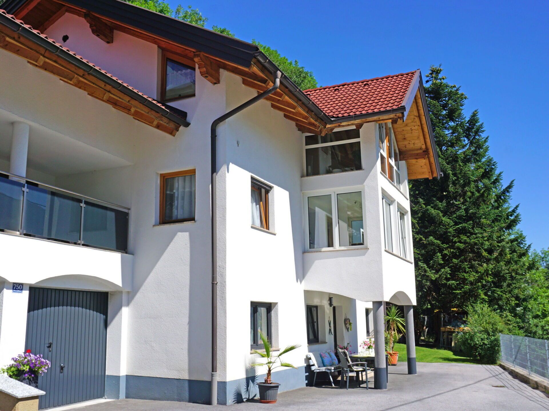 Una casa de dos pisos con balcón, garaje y un patio con mobiliario exterior.