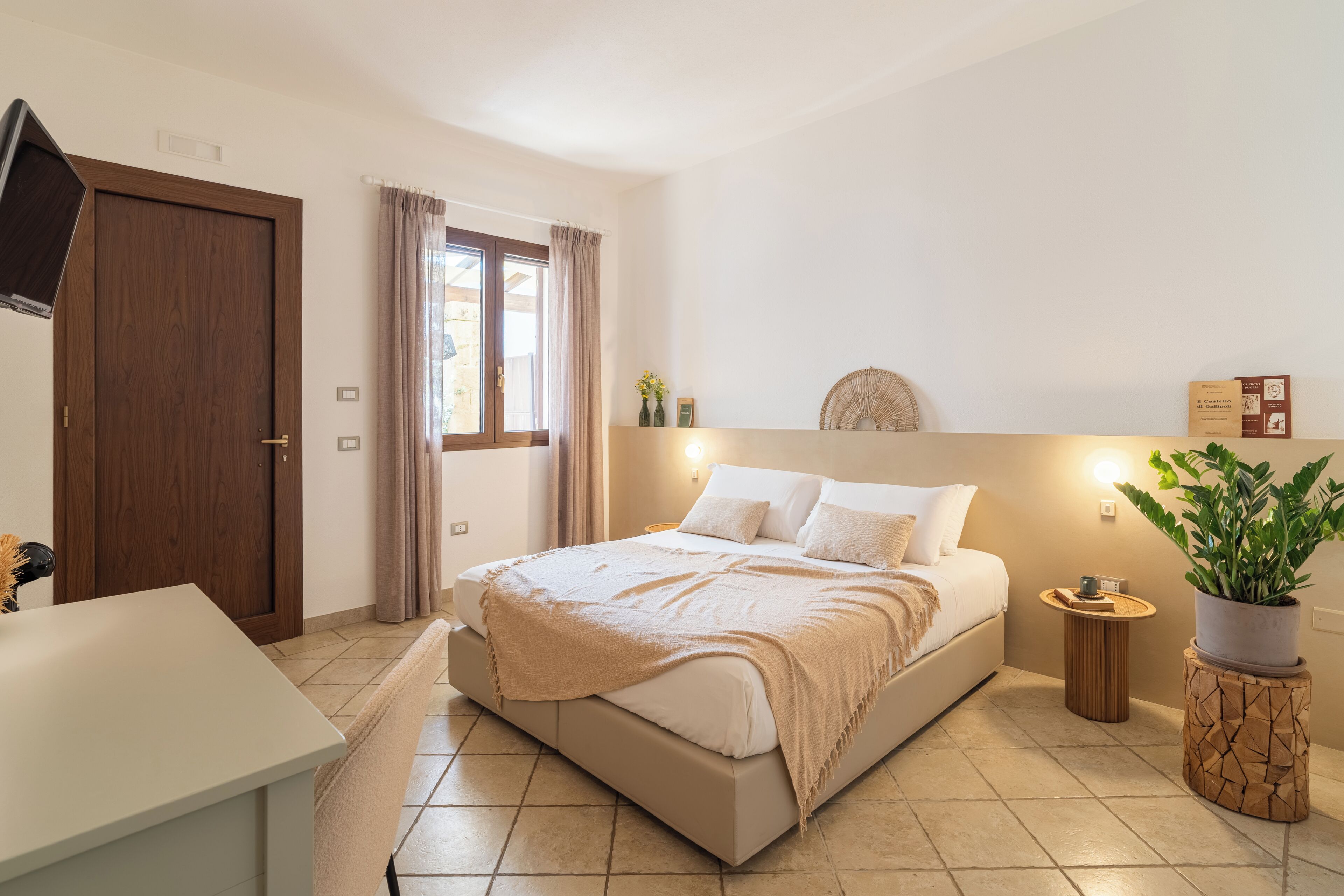 Quarto com cama, mesa de cabeceira, abajur e um vaso com planta.