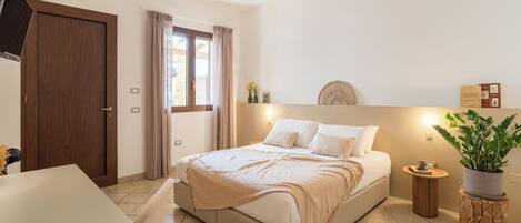 Quarto com cama, mesa de cabeceira, abajur e um vaso com planta.