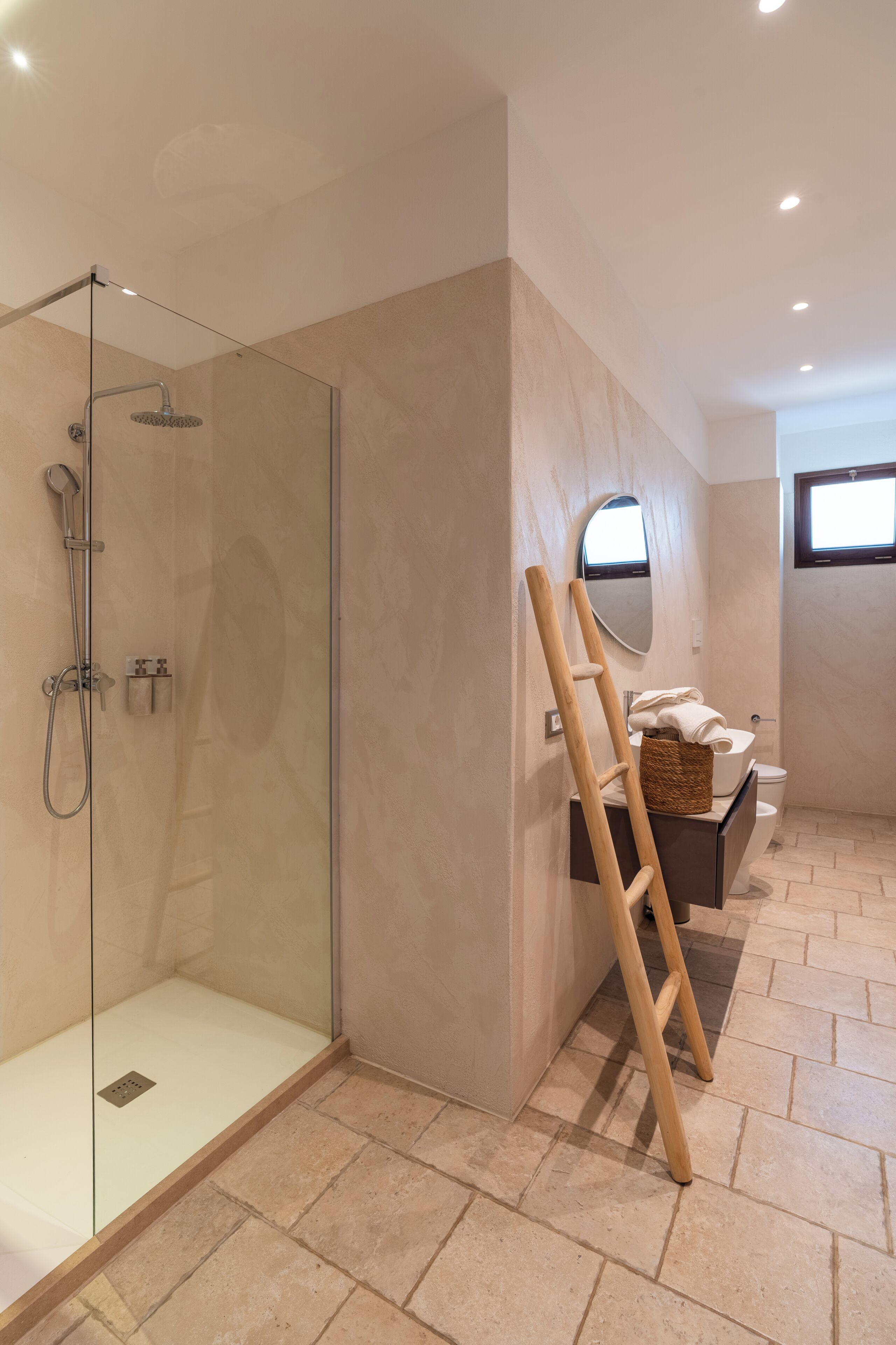 Une salle de bain moderne avec une douche à parois de verre, une échelle en bois, des toilettes et une petite fenêtre.