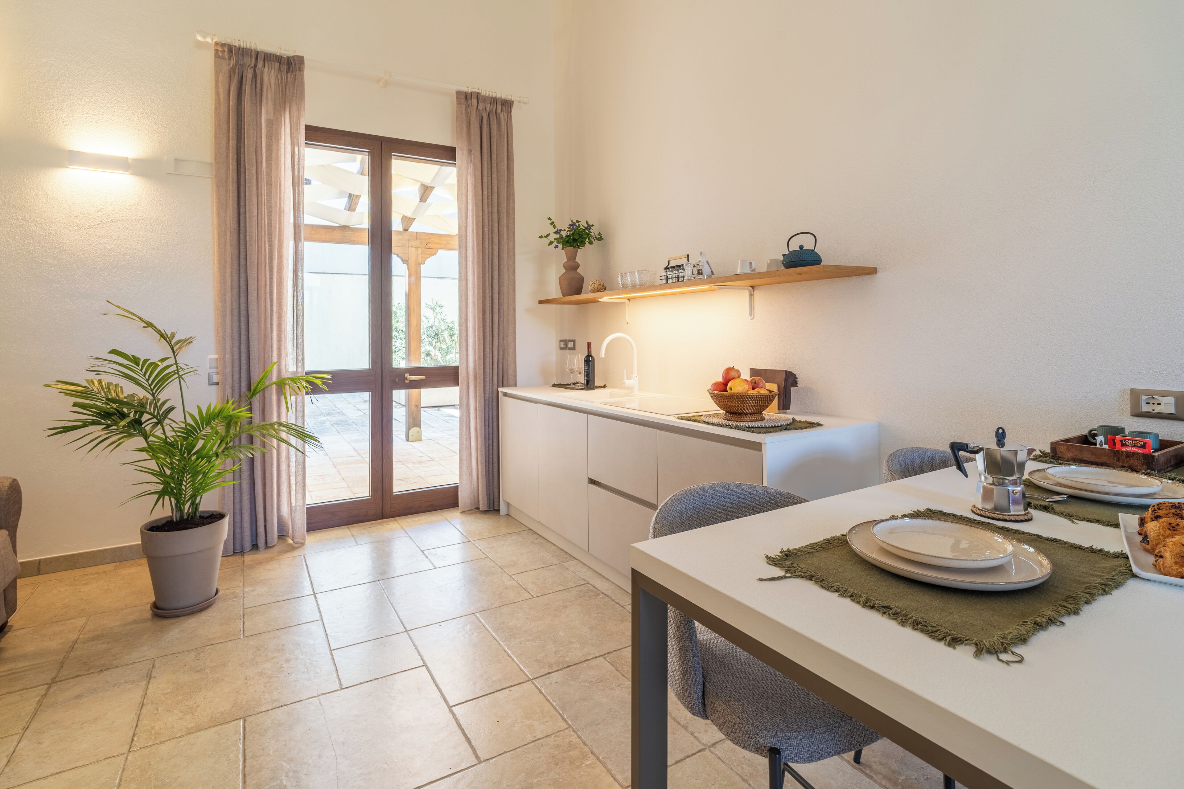 A modern kitchen with a dining area, a potted plant, and a sliding glass door leading to an outdoor area.
