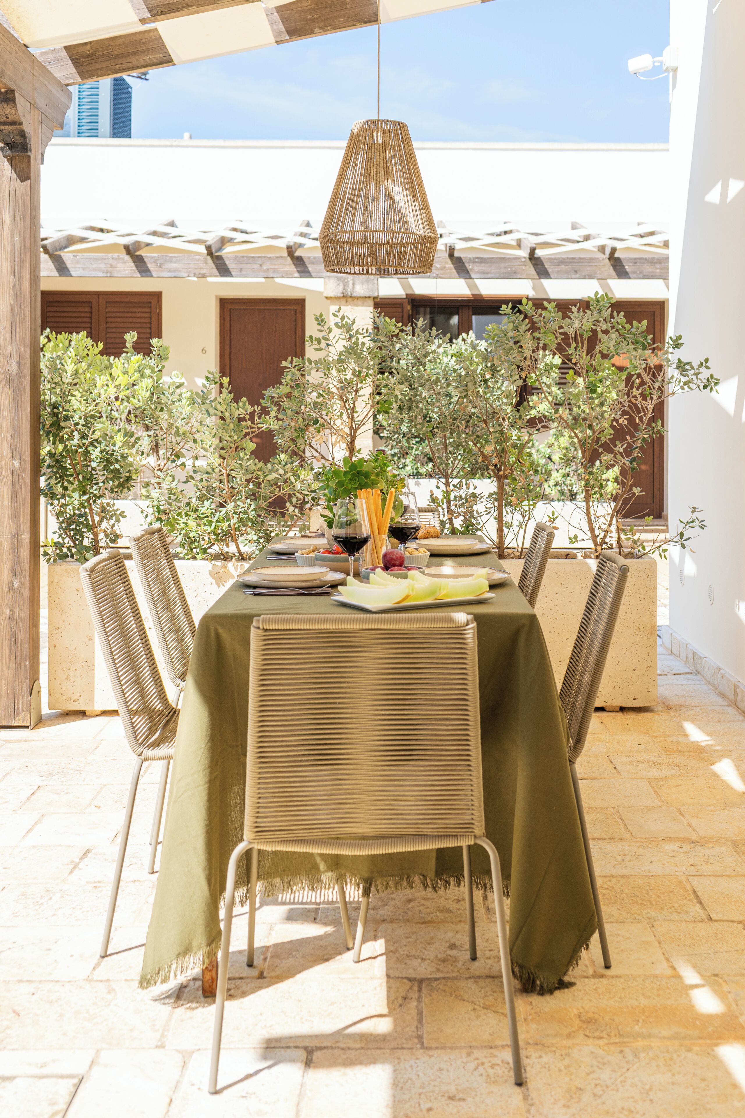 Un espace de restauration en plein air avec une table dressée pour deux personnes, entourée de chaises en osier, sous une tonnelle en fibres tressées.