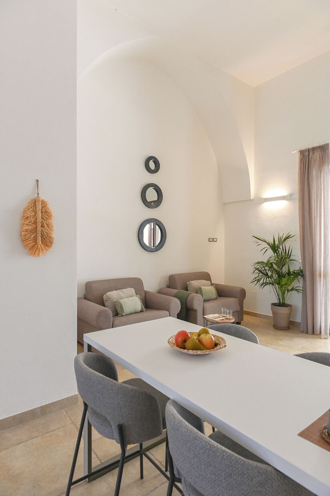 A modern dining area with a white table, grey chairs, and a potted plant.