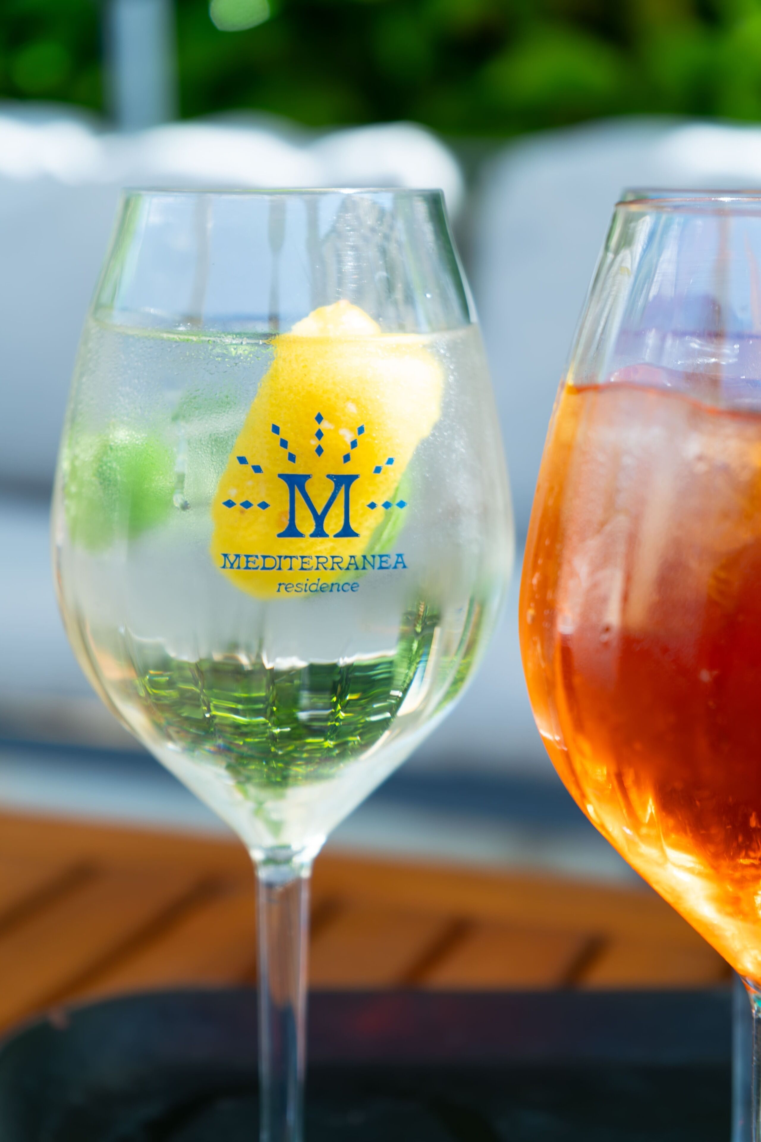 Two glasses of beverages, one with a yellow lemon slice and the other with a red drink, on a table.