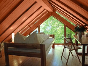 Een gezellig slaapkamer op zolder met een houten schuine dak, een bed met kussens, een stoel en een tafel met een bloevas.