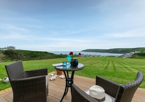Relax in a serene outdoor setting with a round table and two chairs overlooking a lush lawn and the distant coastline.