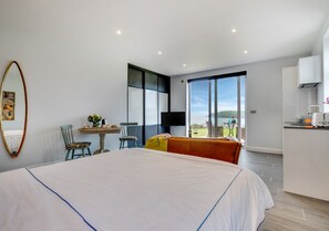 Relax in this stylish room with a large bed, a small table, and a kitchenette area, offering a view of the outdoors through a large window.