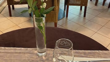 Uma mesa de jantar com um vaso de flores, copos de vinho vazios e talheres.