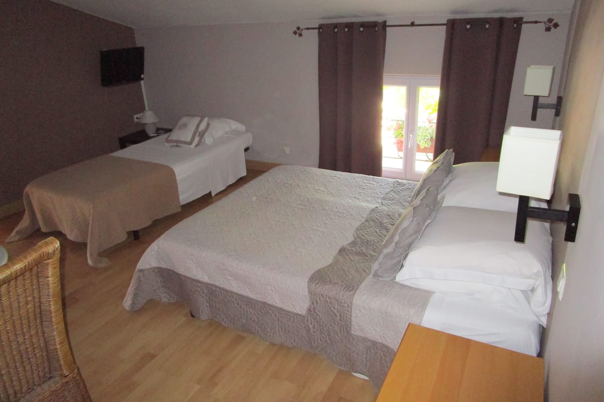 A hotel room with two beds, a wooden floor, a flat-screen TV, and a window with curtains.