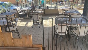 An outdoor patio with wooden tables and chairs, a railing, and a view of the street. - Hotel Restaurant l'Escapade (Bedoin)