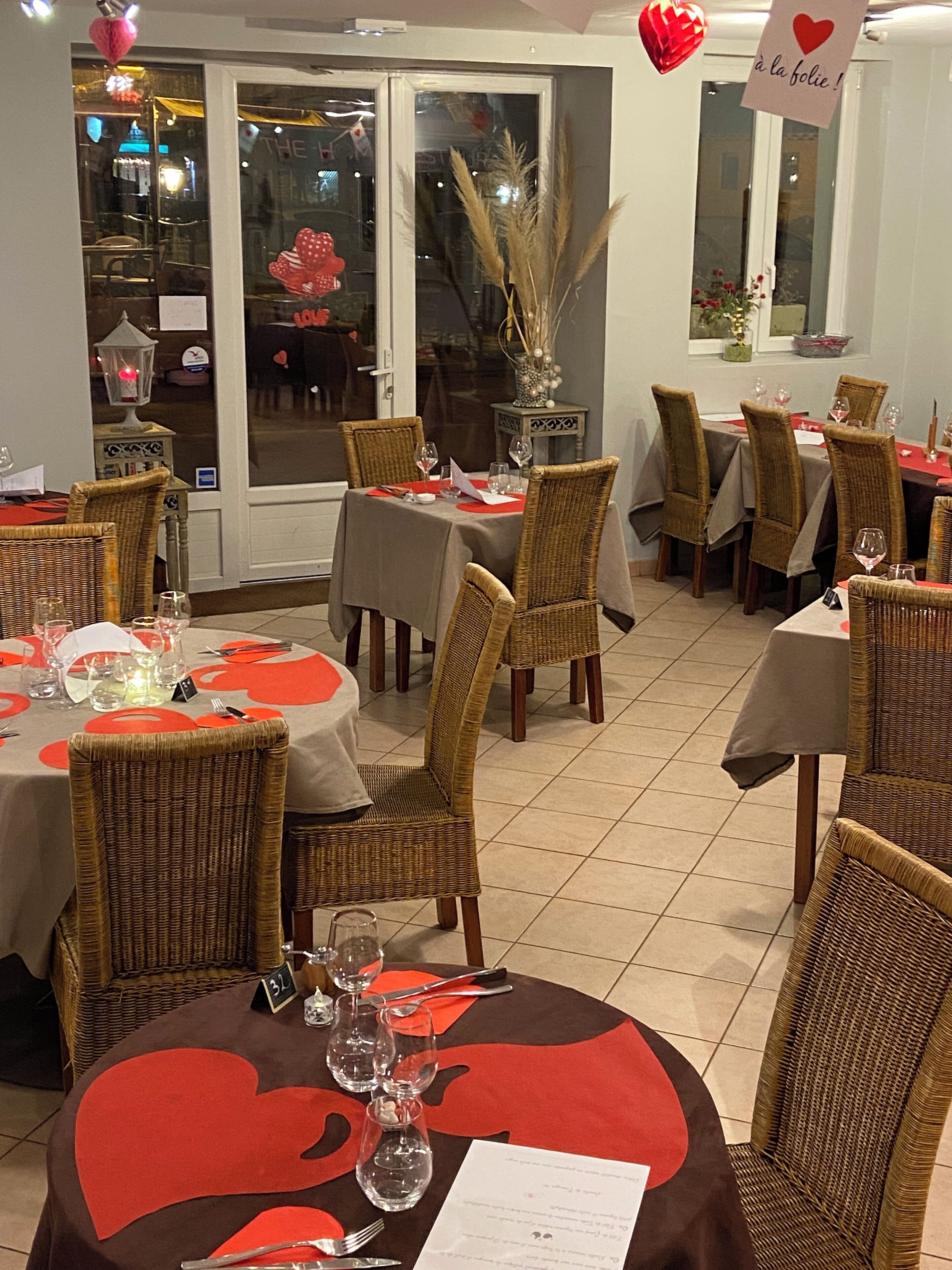 A restaurant interior with multiple tables set for dining, wicker chairs, and a view of the street outside.