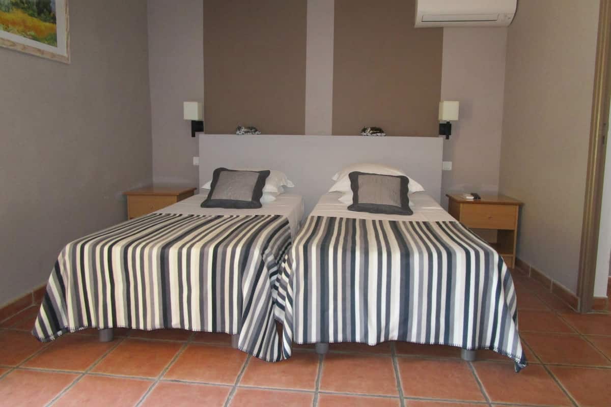 A hotel room with two beds, striped bedding, a headboard, bedside tables, and an air conditioning unit.