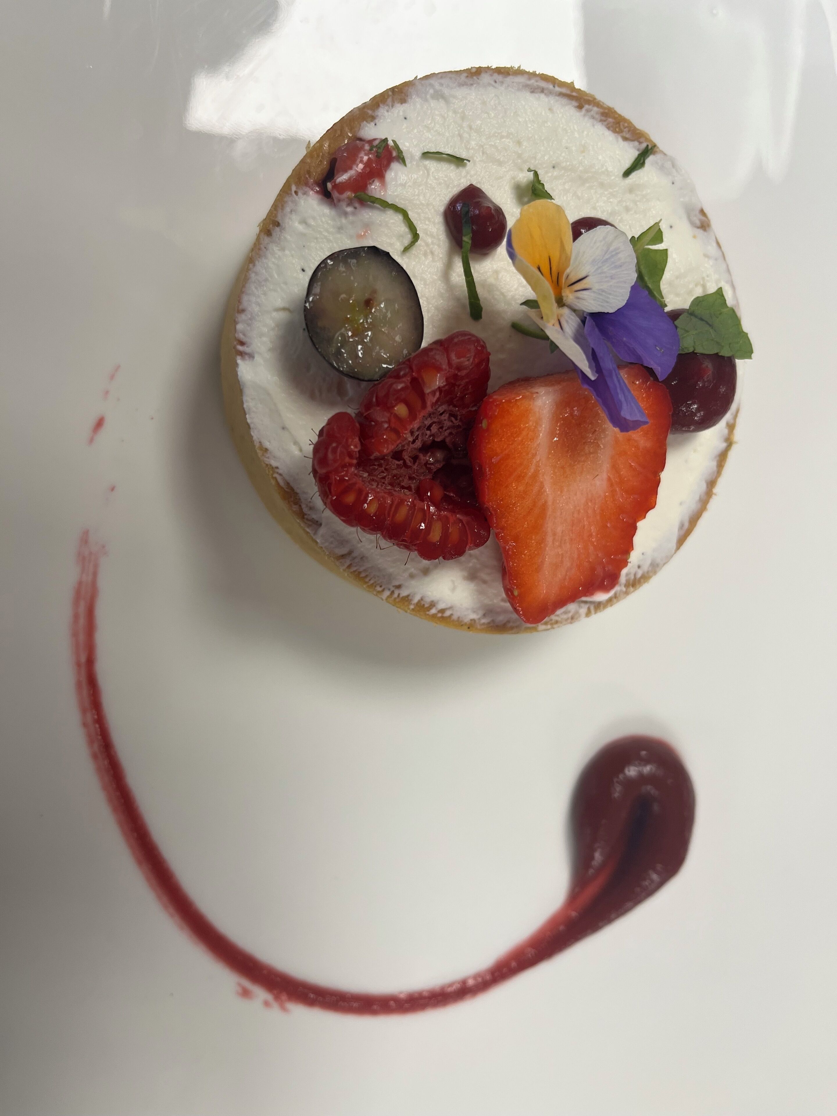 A dessert with various fruits and a flower on a white plate.