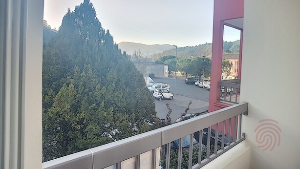 Un balcón con vista a un estacionamiento, árboles y colinas distantes.