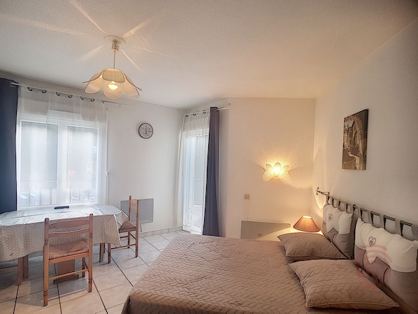 A bedroom with a bed, a desk, a chair, a wall clock, and a painting. - Cozy 24m² Apt, Renovated, Balcony, 650m from Lamalou Thermal Baths, Pets Welcome (Lamalou-les-Bains)