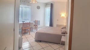 Un dormitorio con cama, una silla, una mesa y una ventana con cortinas.