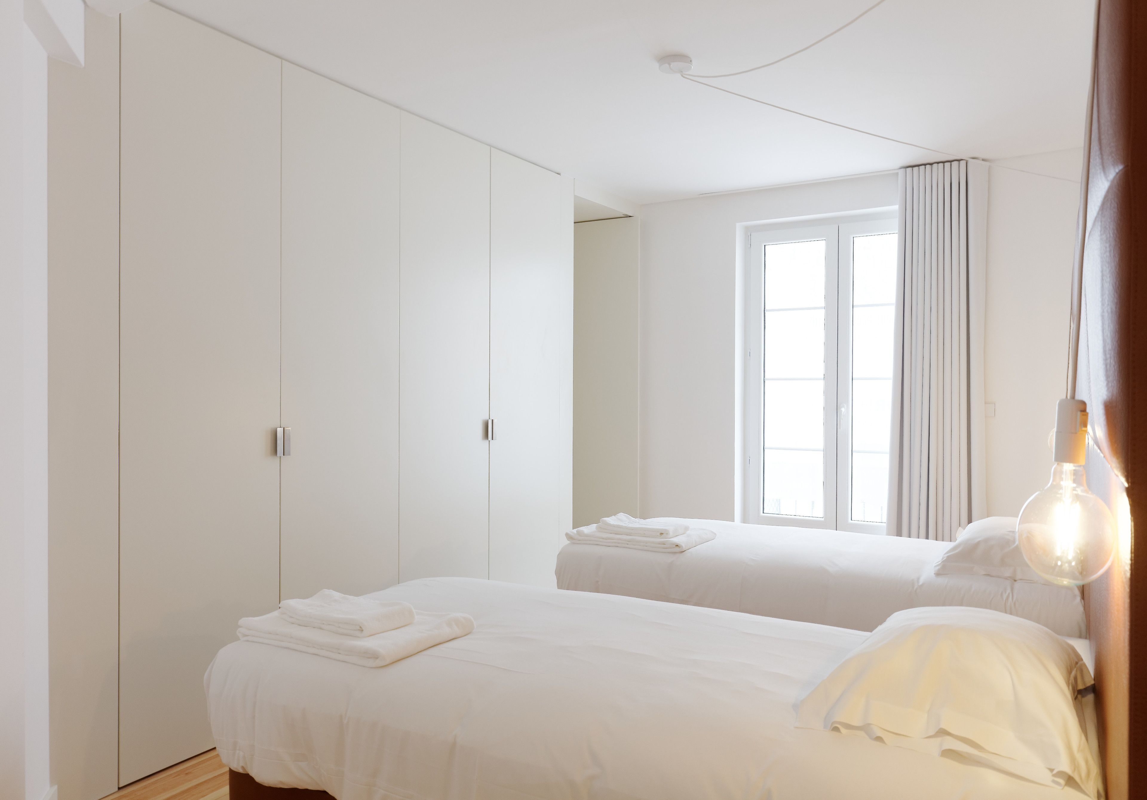 Habitación de hotel con dos camas, un armario, una ventana con cortinas y una lámpara colgante.