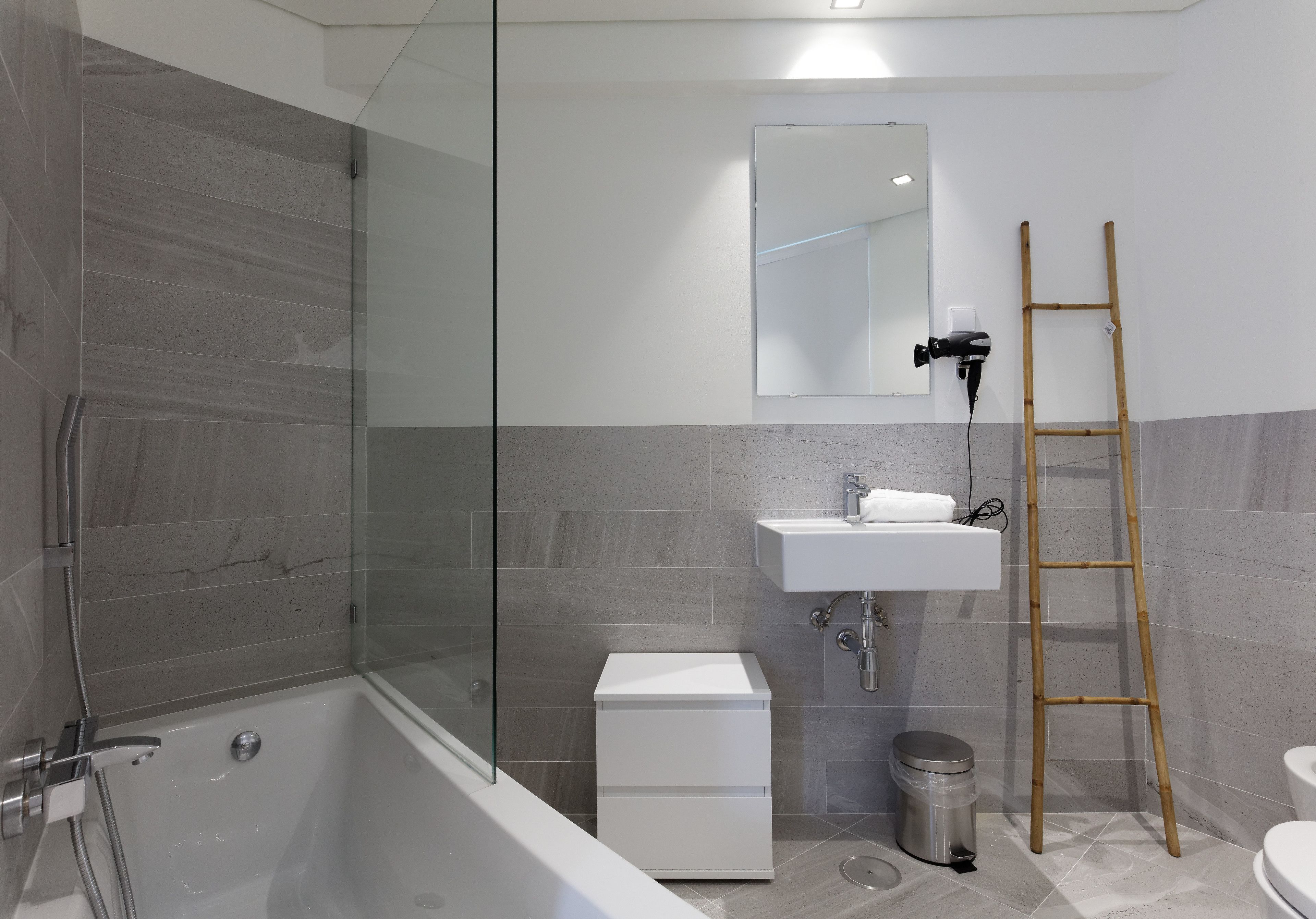 A modern bathroom with a glass-enclosed shower, a white sink, and a wooden ladder.