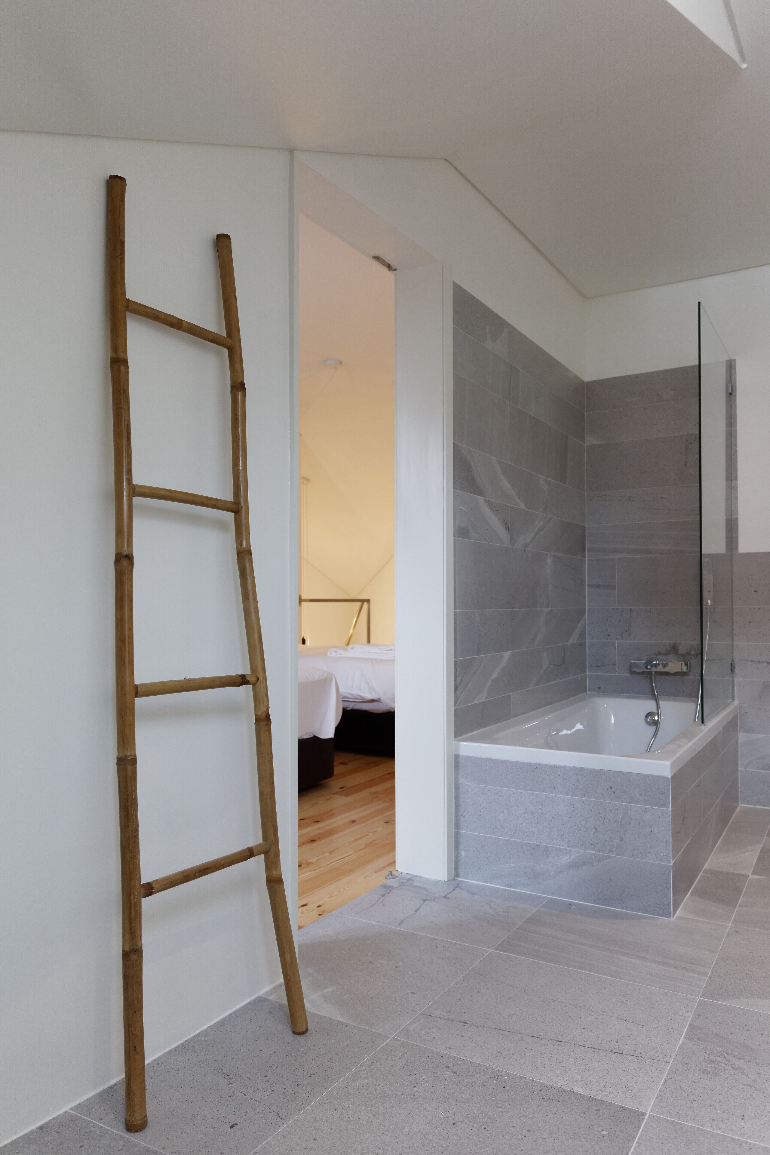 Un bagno moderno con doccia vetrata, una scala in legno e un letto nella stanza adiacente.