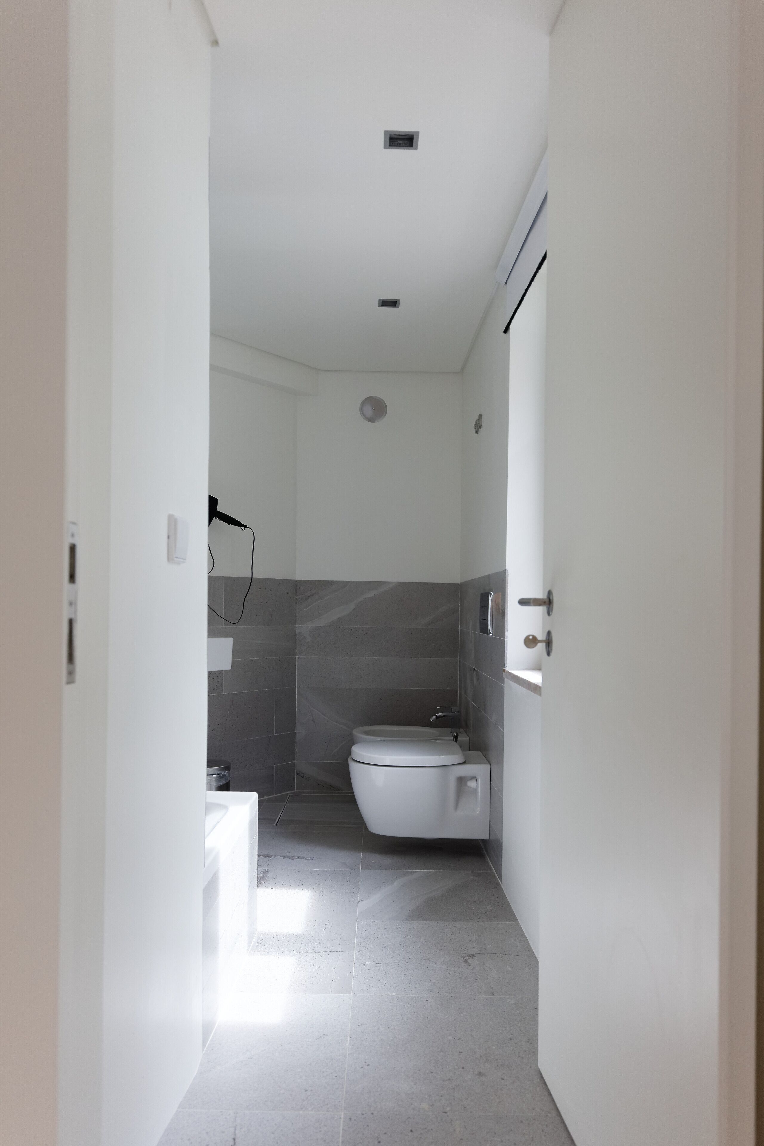 Un couloir étroit mène à une salle de bain équipée de toilettes et d’un espace douche.
