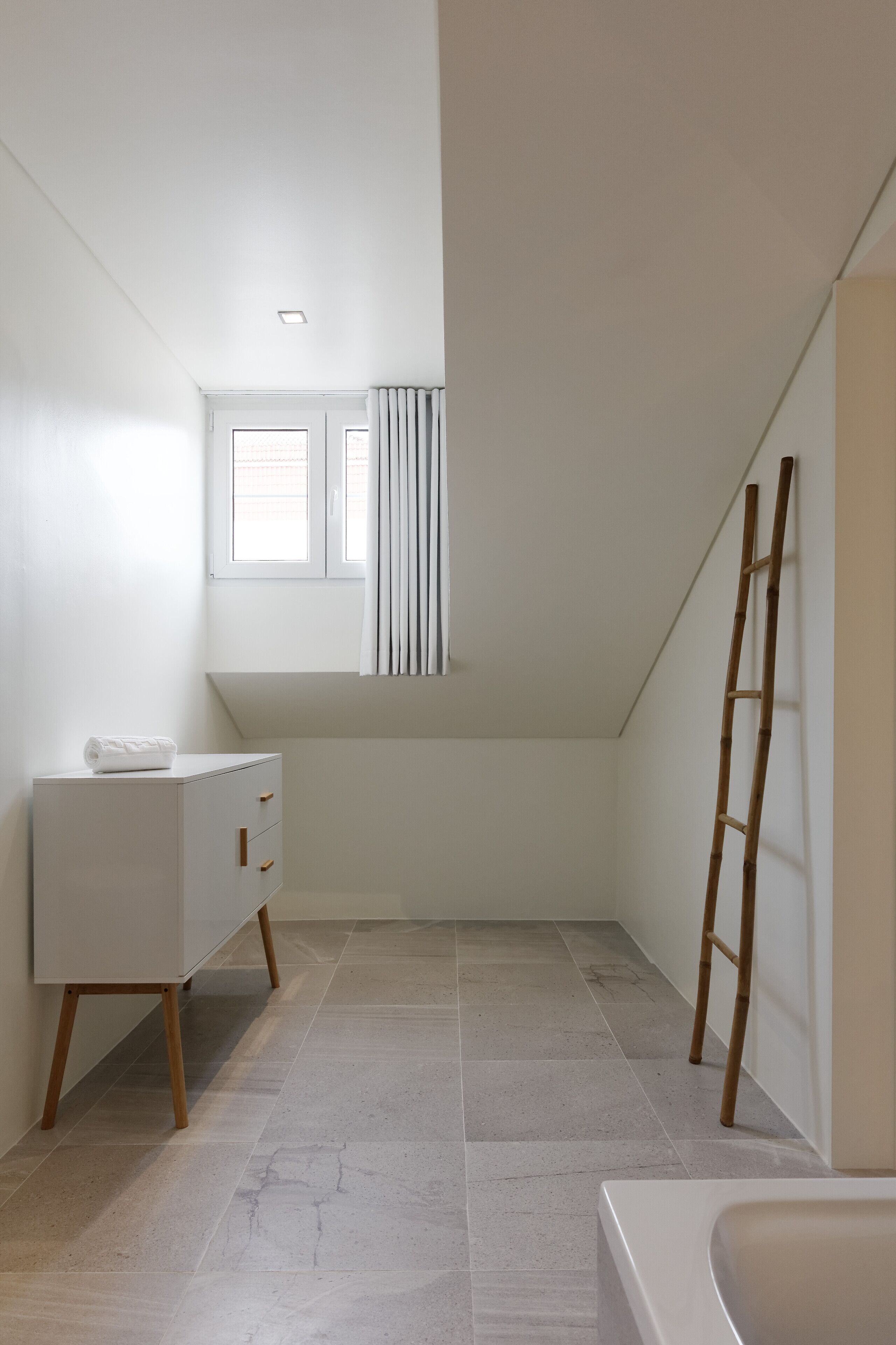 A modern bathroom with a white vanity, a bathtub, and a window with curtains.