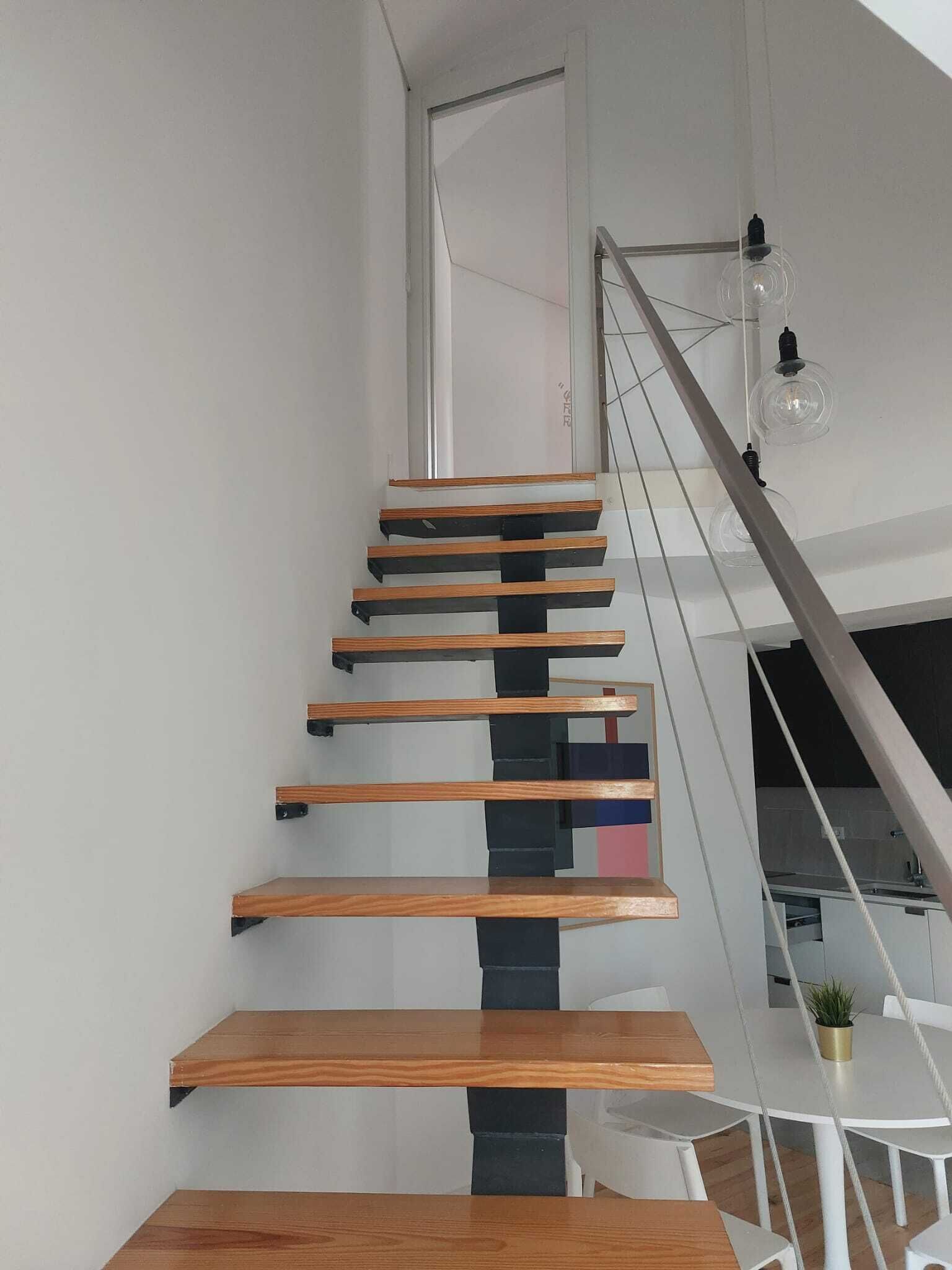 Una escalera moderna con escalones de madera y soportes negros que conduce a una puerta blanca.