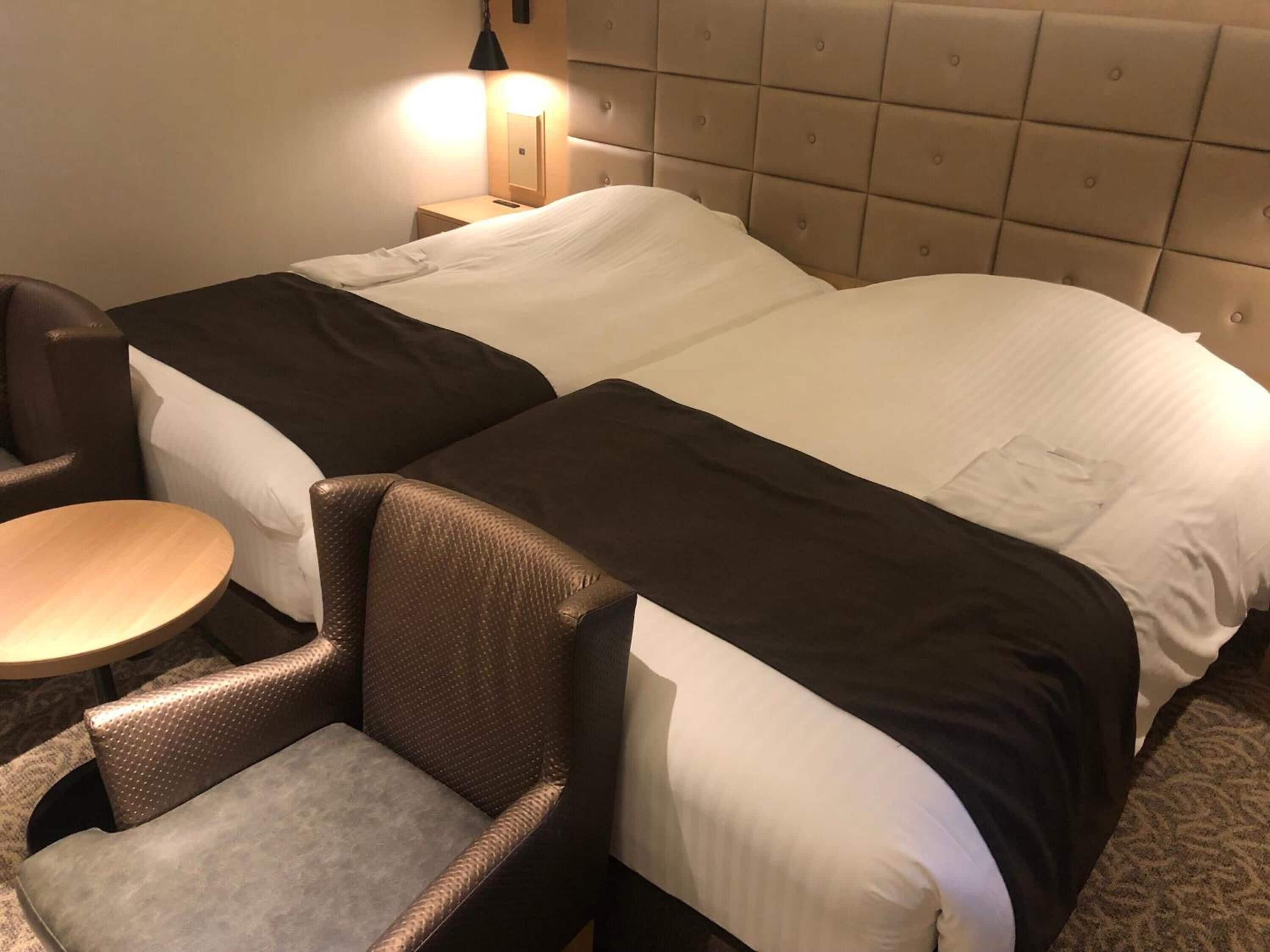 A hotel room with two beds, a small round table, and a chair.