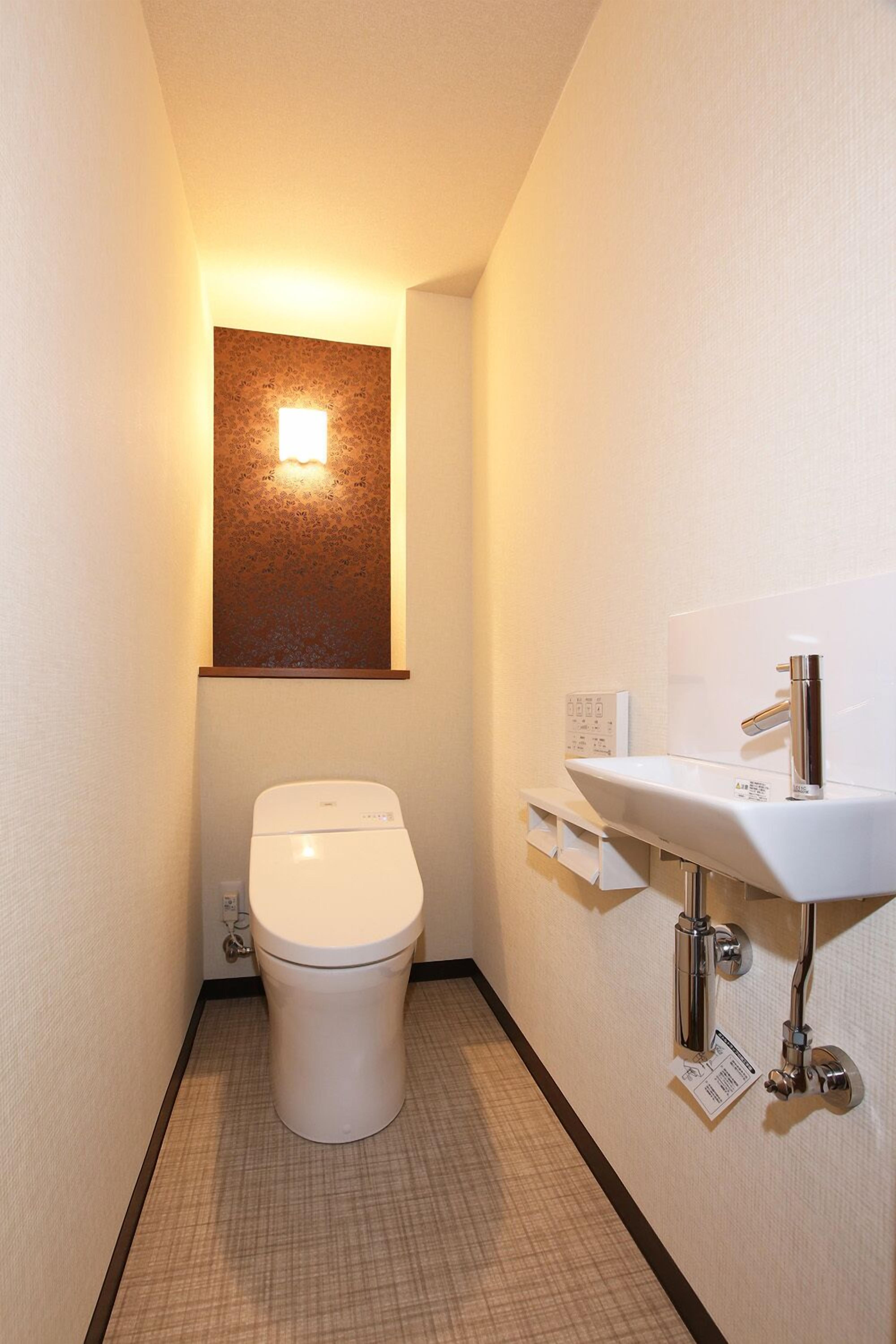 A small, narrow bathroom with a white toilet, a wall-mounted sink, and a light fixture above the toilet.