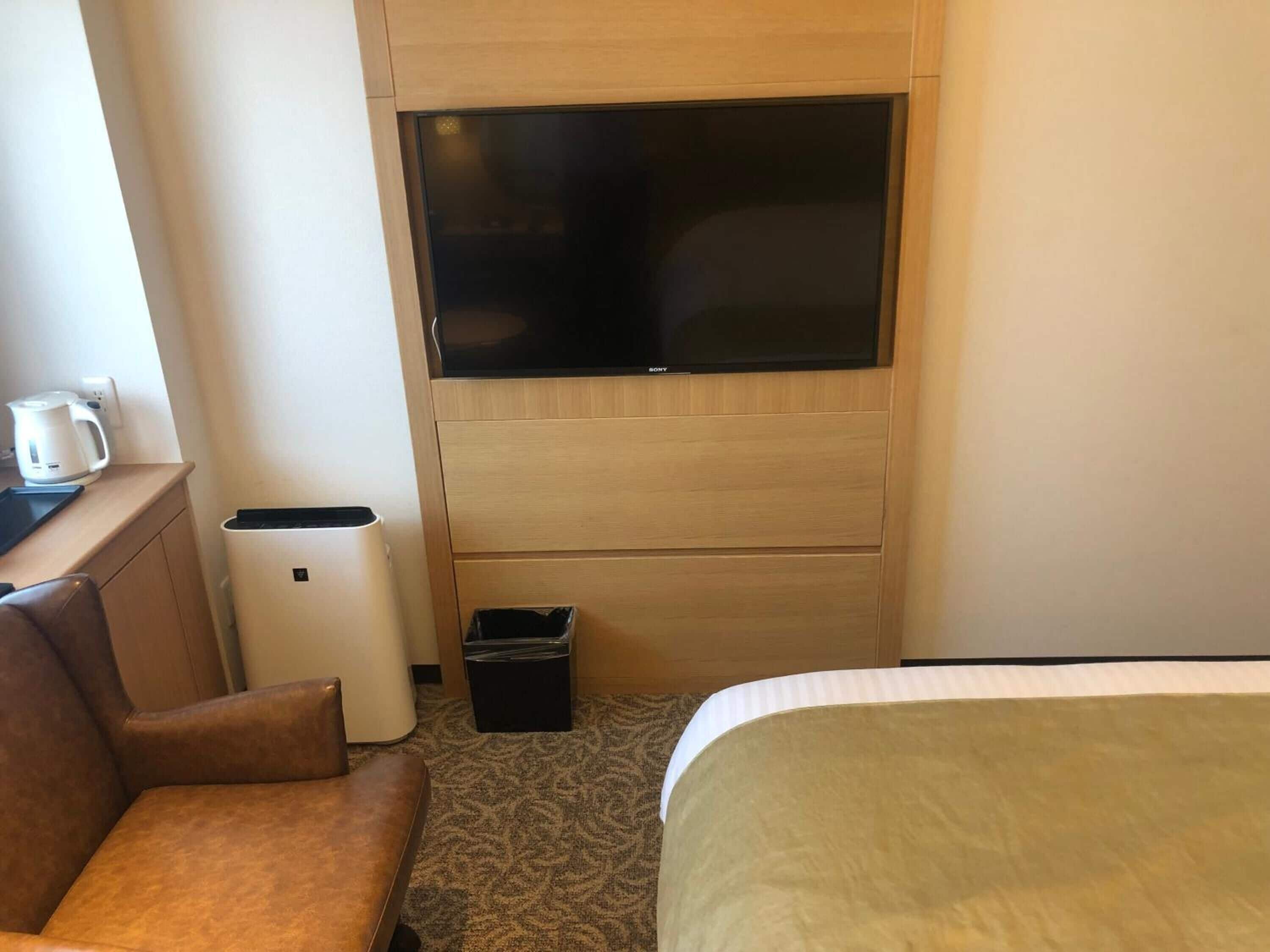 Ein Hotelzimmer mit Bett, einer Couch, einem Fernseher, einer Kaffeemaschine und einem Mülleimer.