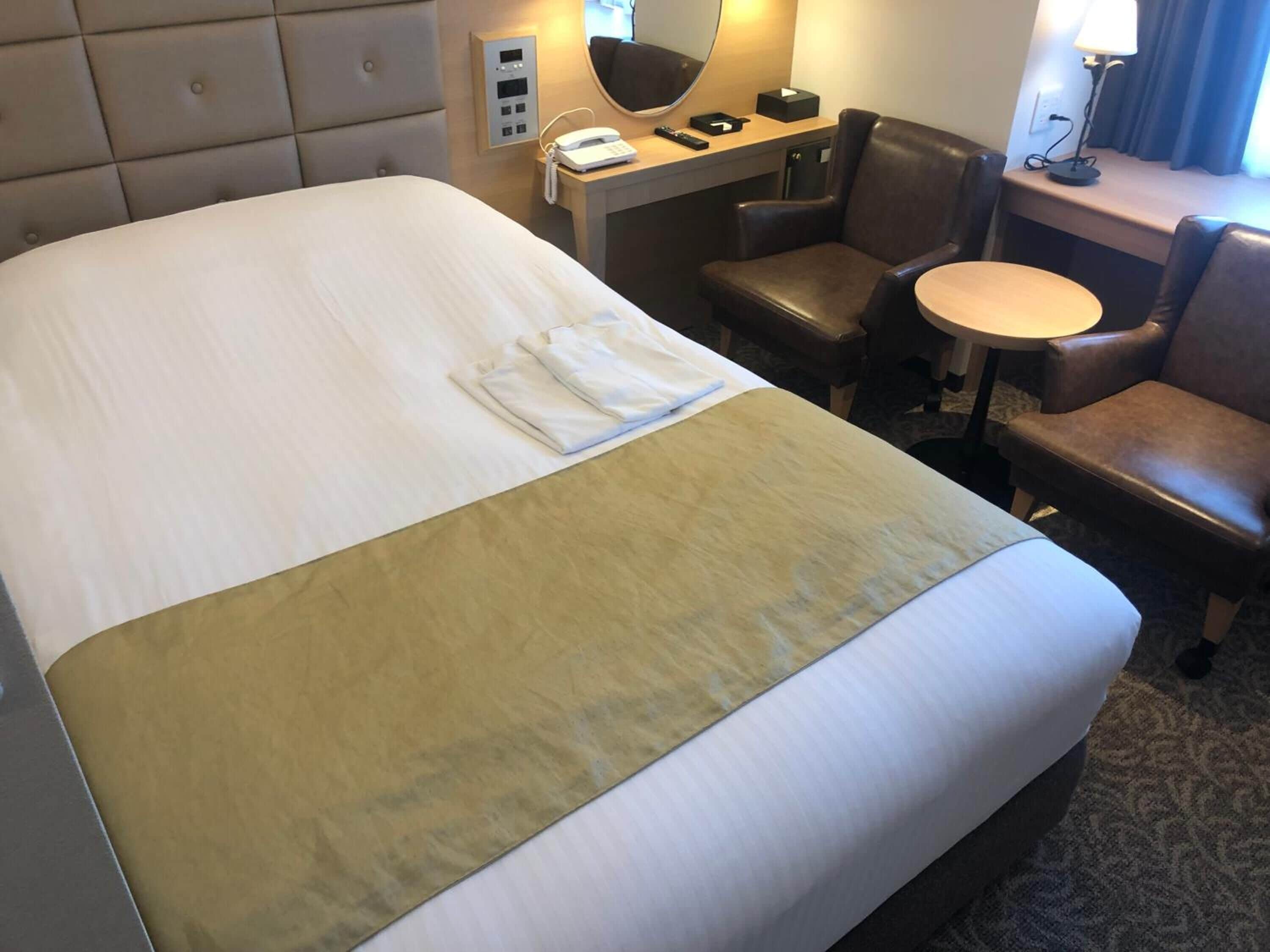 Una habitación de hotel con una cama grande, un escritorio con teléfono, una silla y una mesita.