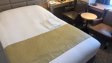 Una habitación de hotel con una cama grande, un escritorio con teléfono, una silla y una mesita.